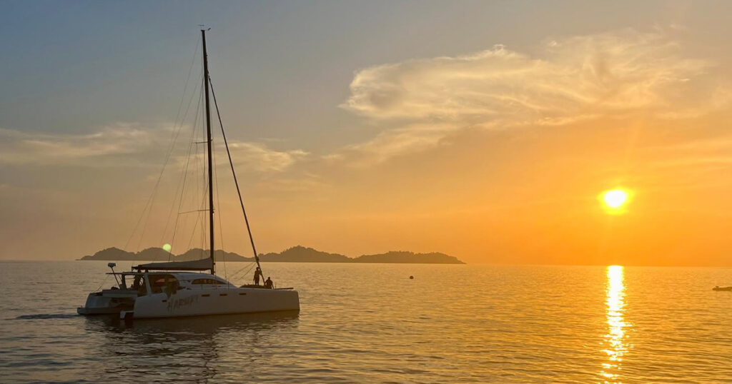 Stealth catamaran anchored at sunset off a tropical island beach in Thailand