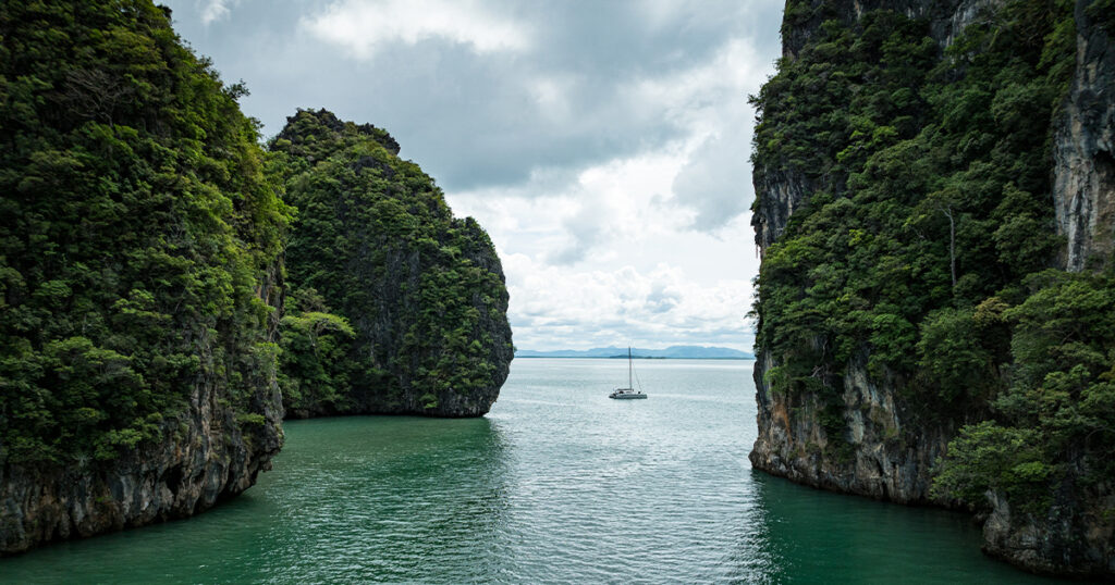 Stealth catamaran Haruki sailing between limestone cliffs at Ko Talabeng Thailand